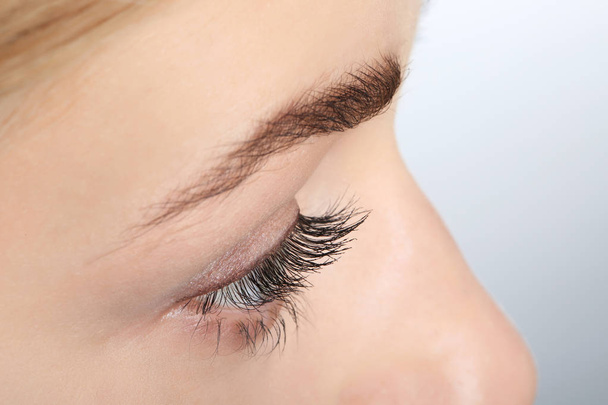 Young woman with beautiful natural eyelashes on light background, closeup view - 写真・画像