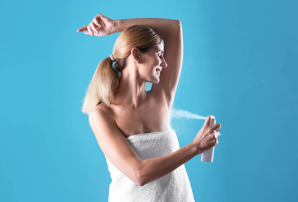 Young woman using deodorant on color background - Zdjęcie, obraz
