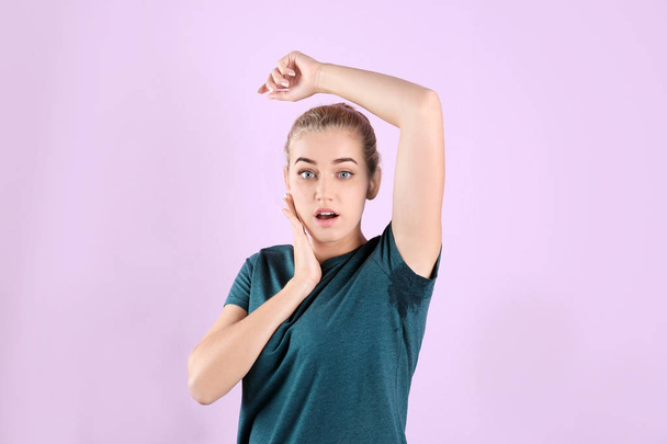 Young woman with sweat stain on her clothes against color background. Using deodorant - Foto, immagini