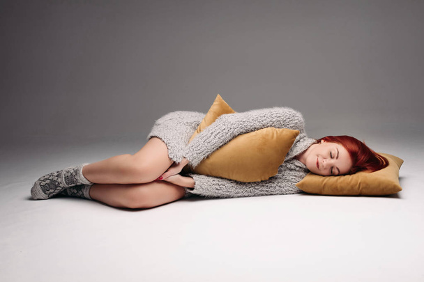 Studio portrait of a woman in a sweater hugging a pillow. - Photo, image
