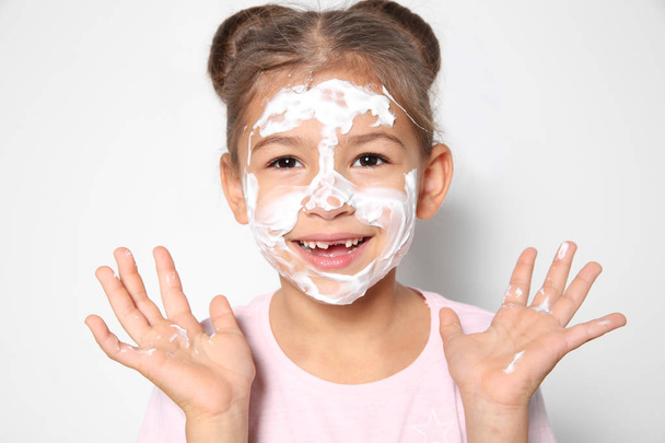 Cute little girl with soap foam on face against white background - Fotó, kép