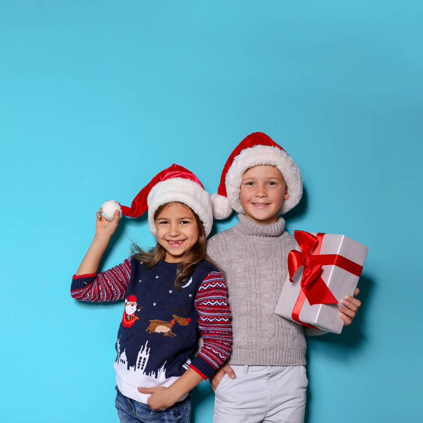 Cute children in warm sweaters and Christmas hats and gift on color background - Photo, image