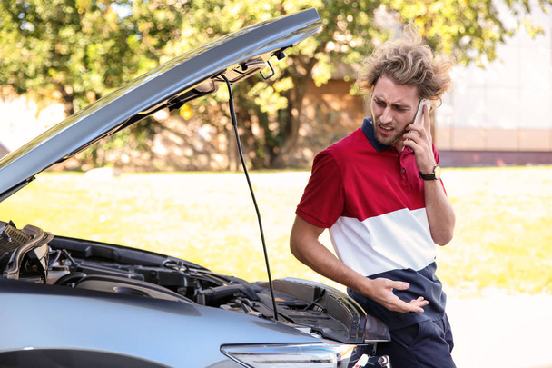 Young man talking on phone near broken car, outdoors - Foto, imagen