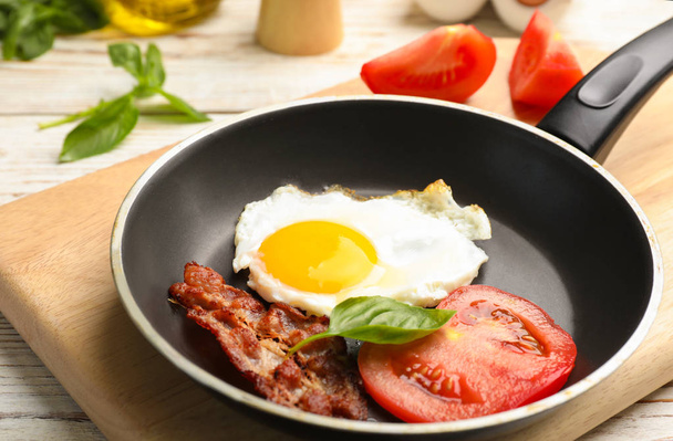 Pan with fried sunny side up egg, bacon and tomato on table - Φωτογραφία, εικόνα