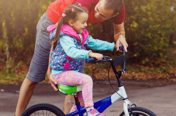 Padre insegnamento figlia a cavalcare bici in parco
 - Foto, immagini