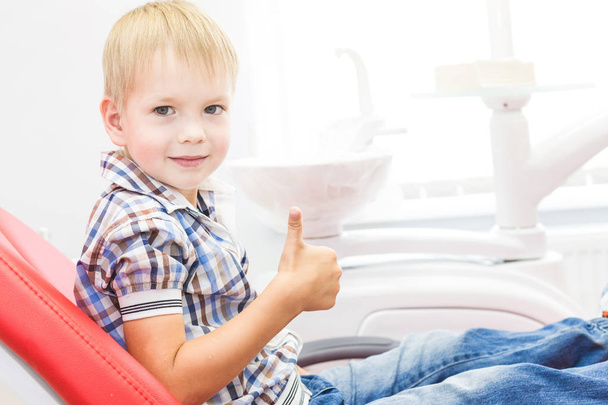 Zubní klinika. Příjem, vyšetření pacienta. Péče o zuby. Malý chlapec ukazuje palcem nahoru podepsat v kanceláři lékaři - Fotografie, Obrázek