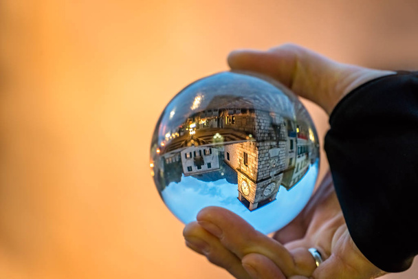 Uomo che tiene la palla di vetro trasparente che riflette la vecchia torre dell'orologio e la piazza nella città vecchia di Kotor, Montenegro
 - Foto, immagini