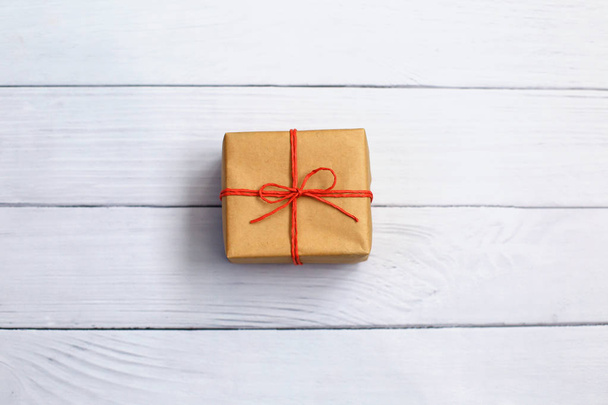 Caja de regalo envuelta en papel reciclado con hilo rojo sobre fondo de madera
. - Foto, imagen