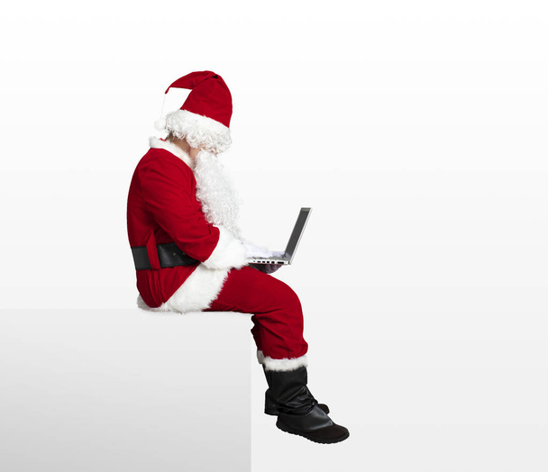 サンタ クロースのノート パソコンを見ているとブランク パネルの上に座って  - 写真・画像