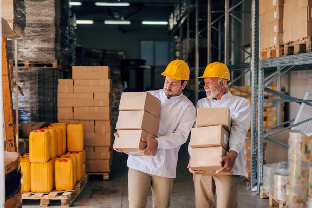 Image de deux ouvriers d'entrepôt avec des casques sur la tête portant des boîtes dans leurs mains
 - Photo, image