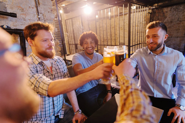 junge glückliche bärtige Männer feiern und stoßen mit Bier in der Kneipe an - Foto, Bild