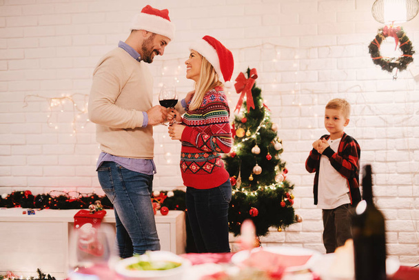 familia feliz celebrando la Navidad en casa, los padres bebiendo vino cerca del árbol de Navidad
  - Foto, Imagen