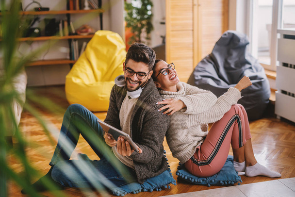 Šťastný pár sedící zády k sobě na podlaze v obývacím pokoji při používání tabletu. - Fotografie, Obrázek