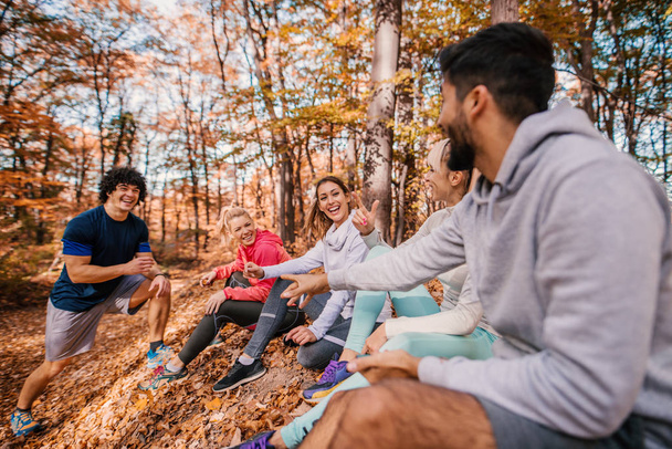 Groep lopers zitten en chatten na het lopen. Bos in de herfst buitenkant. Teamwork en gezonde levensstijl concept. - Foto, afbeelding
