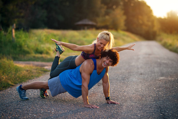 Samen trainen is leuker. Jonge knappe man doet push ups terwijl zijn vriendin op zijn rug zit. - Foto, afbeelding