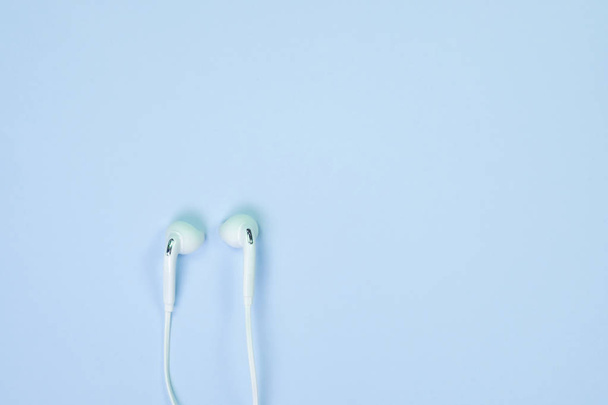 White Earphones or ear buds small talk on sweet blue colour pastel paper, top view, texture and background. music listening concept idea. - Fotó, kép