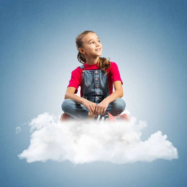 Cute kid girl sitting on cloud against blue color background - Photo, Image
