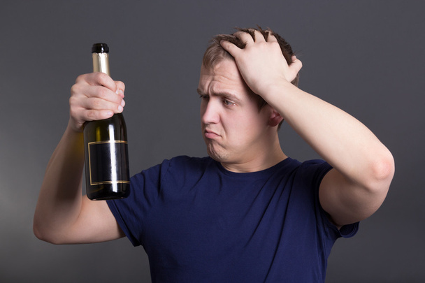 jeune homme ivre avec bouteille de champagne sur gris - Photo, image
