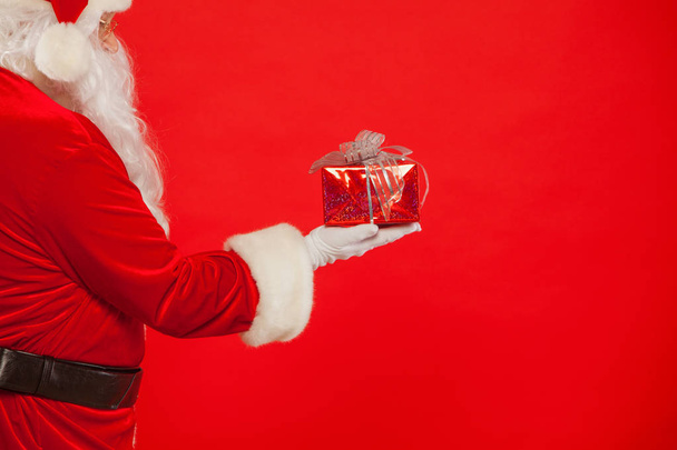 Photo of Santa Claus gloved hand with giftbox, on a red backgrou - Foto, Imagem