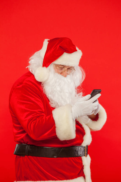 Photo of Santa Claus using mobile phone, on a red background. Christmas. - Foto, Imagem