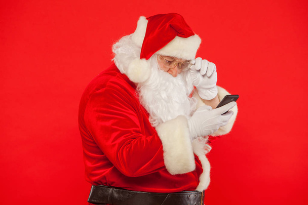 Photo of Santa Claus using mobile phone, on a red background. Ch - Фото, зображення