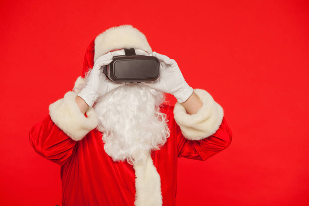 Santa Claus wearing virtual reality goggles, on a red background - Fotoğraf, Görsel