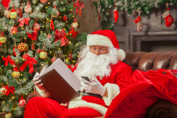 Santa Claus sitting at his home in a comfortable chair and readi - 写真・画像