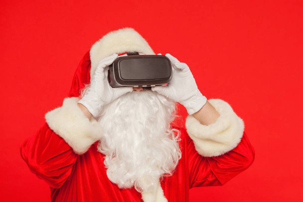 Santa Claus wearing virtual reality goggles, on a red background - Fotoğraf, Görsel