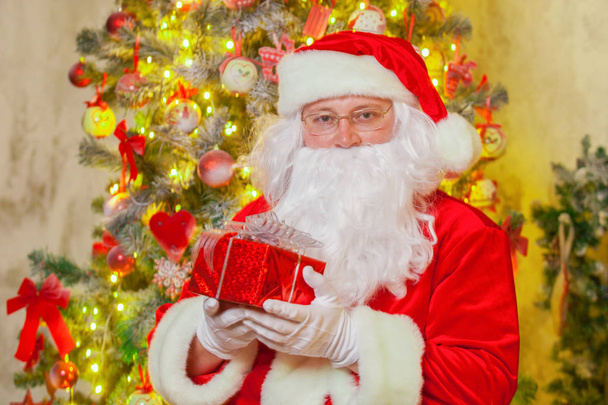 Santa Claus with giftbox on background of sparkling firtree - Fotoğraf, Görsel