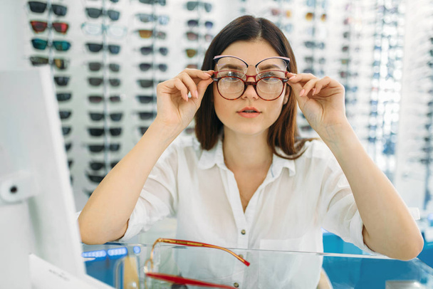 女性のバイヤーは、同時に、光学ストアの背景に眼鏡とショーケース多くのメガネにしようと。専門クリニック、眼鏡店 - 写真・画像