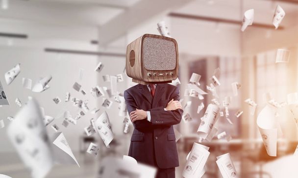 Cropped image of businessman in suit with old TV instead of head keeping arms crossed while standing among flying papers inside office building. - Фото, изображение