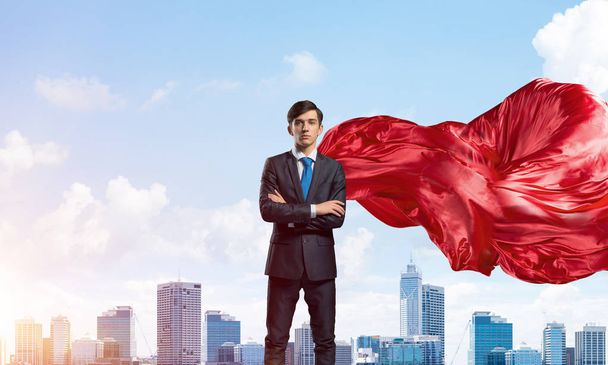 Joven hombre de negocios confiado usando capa roja contra el fondo moderno de la ciudad - Foto, imagen