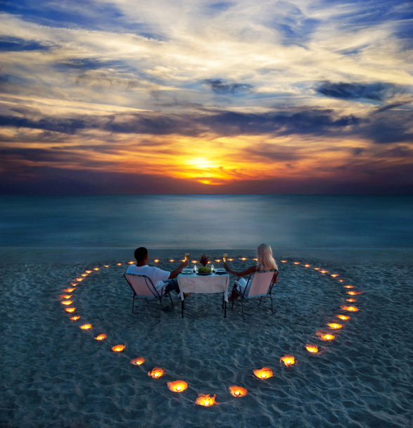 een jong koppel delen een romantisch diner op het strand - Foto, afbeelding