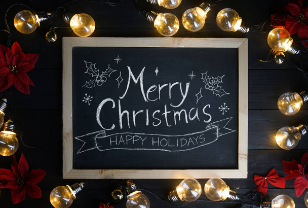 Joyeux Noël Typographie sur tableau noir entre les ampoules et Poinsettia rouge sur bois noir
 - Photo, image