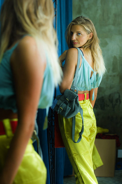 young beautiful and happy blond woman enjoying shopping trying out clothes in the mirror at vintage and cool beauty fashion store smiling cheerful having fun buying sales and opportunity clothing - Photo, image