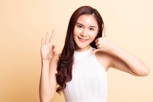 Young Asian woman show with phone gesture and OK sign   on beige background. - Foto, Bild