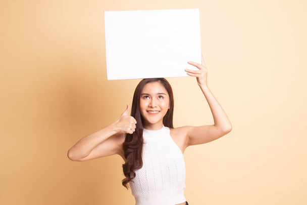 Young Asian woman show thumbs up with white blank sign   on beige background. - Foto, immagini