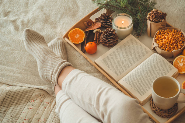 Acogedora noche de invierno, cálidos calcetines de lana. La mujer está acostada con los pies sobre una manta blanca y peluda y leyendo un libro. Acogedora escena de ocio
 - Foto, imagen