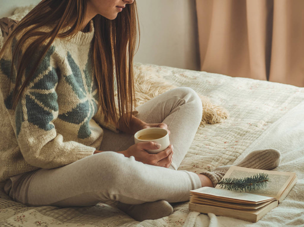 居心地の良い家。美しい少女は、ベッドで本を読んでいます。お茶でおはようございます。リラックスできるきれいな若い女の子。読書の概念 - 写真・画像