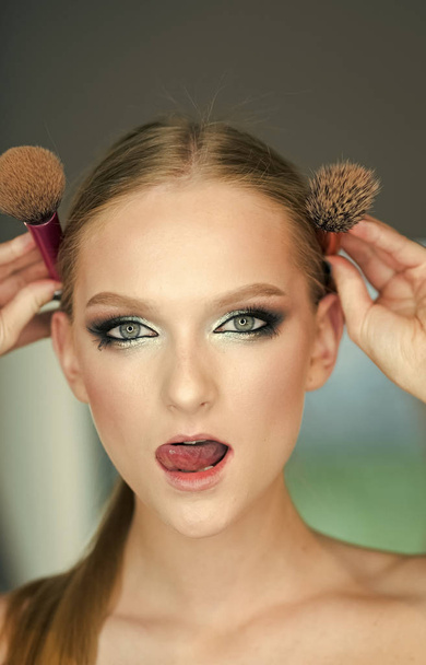 Girl with young skin face, skincare, youth. Woman with makeup face hold brushes at head. Woman with blond hair and makeup brushes, beauty. Beauty model with glamour look, hairstyle - Photo, Image