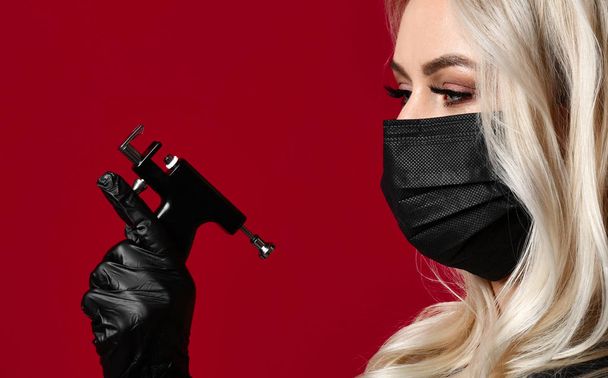 Woman beautician cosmetologist hold new popular ear piercing gun in black medical gloves and mask - Foto, Imagem