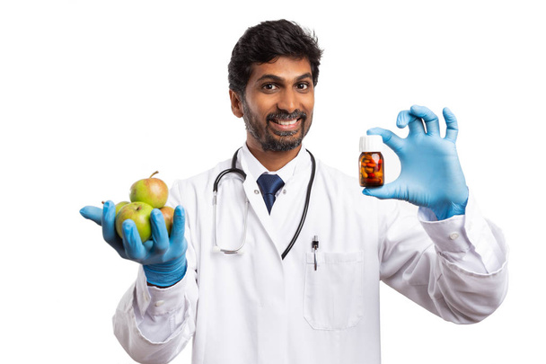 Indien médecin homme avec expression amicale présentant pommes et bouteille de drogue comme mode de vie sain ou concept de régime isolé sur fond blanc
 - Photo, image
