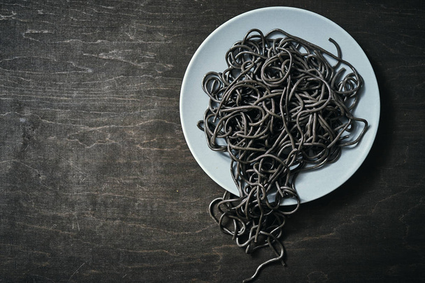 cooked black spaghetti pasta on a gray plate on a black table - Foto, Imagem