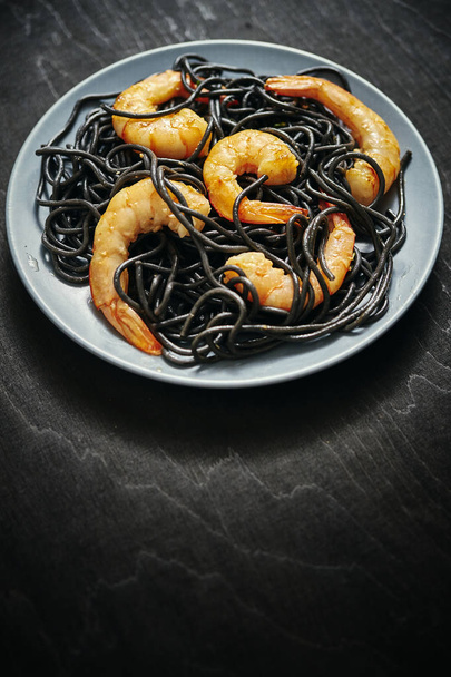φρέσκα, νόστιμα μαύρο Σπαγγέτι με Γαρίδες σχάρας τίγρεις σε ένα γκρίζο πιάτο σε έναν μαύρο πίνακα - Φωτογραφία, εικόνα