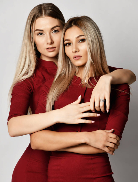 Two beautiful young european sisters friends or girlfriends women in red dresses with clean skin - Foto, afbeelding