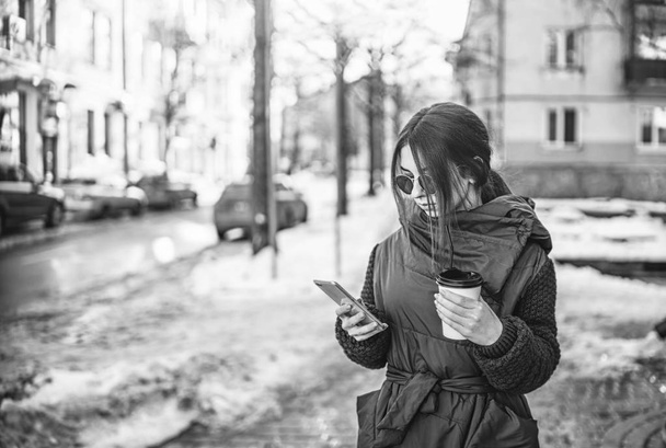 Pretty girl walking on the street with phone and hot drink - Фото, изображение