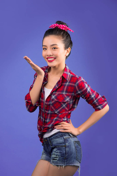 Smiling lovely asian woman dressed in pin-up style gesturing on lilac background - Photo, Image
