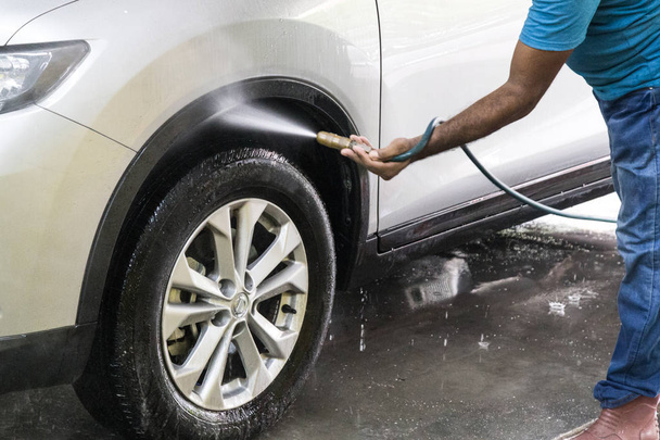 Працівник розбризкує воду на автомобіль для миття в гаражі
 - Фото, зображення