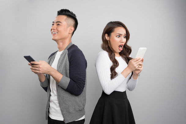 Onnellinen nuori pari innoissaan käyttäessään matkapuhelimia harmaalla taustalla
 - Valokuva, kuva