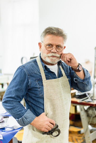 artesano masculino de mediana edad en delantal mirando a la cámara y posando en el taller
 - Foto, Imagen